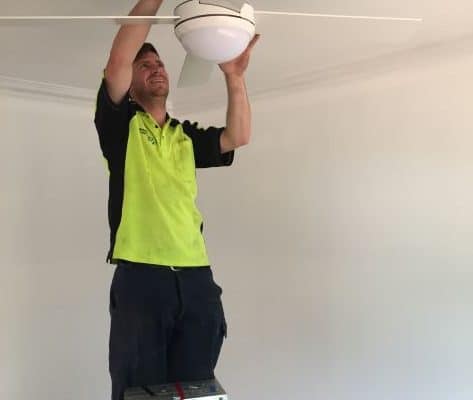Residential Electrician installing a white ceiling fan with a light.