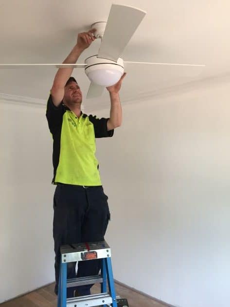 Electrician installing a white ceiling fan with a light.