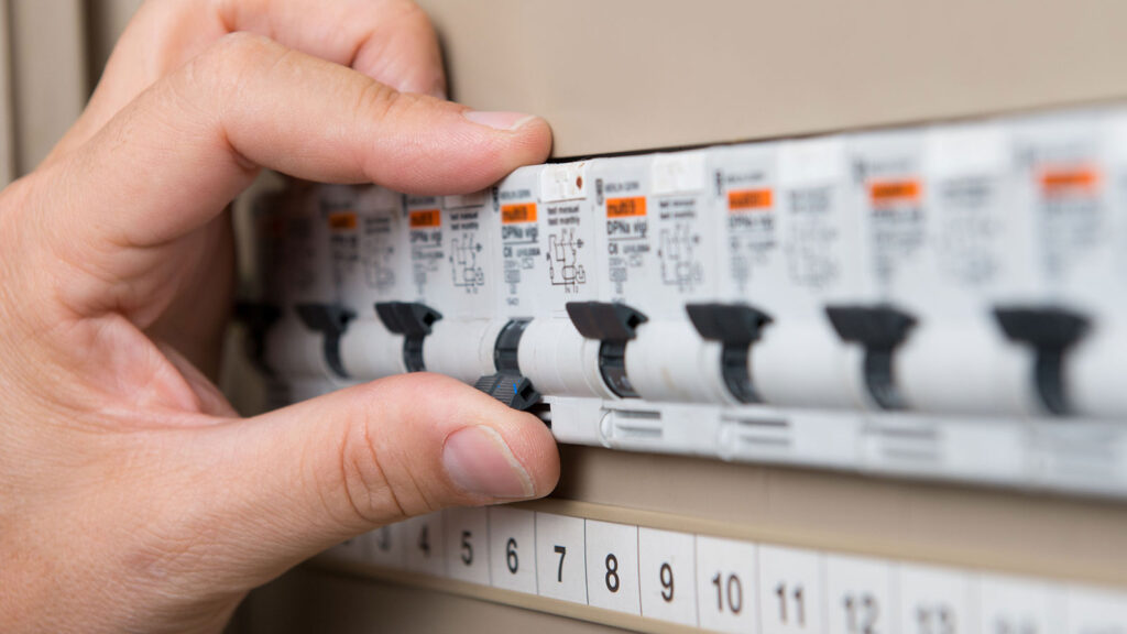 A licensed electrician inspecting a switchboard panel in a Sydney home, checking safety switches and circuit breakers before an upgrade.