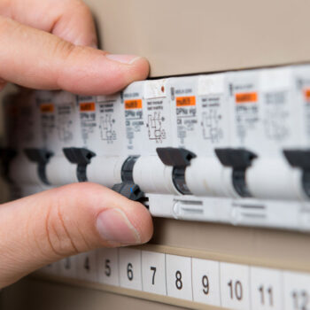 A licensed electrician inspecting a switchboard panel in a Sydney home, checking safety switches and circuit breakers before an upgrade.